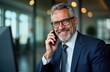 © miss irine - Mature businessman in modern office setting speaks on phone. Appears pleased with positive work results. Successful entrepreneur enjoys successful communication. Formal business environment.