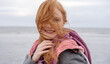 © ullision - Joyful redhead woman at the St. Peter Ording beach, her hair playfully blown by the wind, wrapped in a cozy scarf, exuding happiness and natural beauty against a serene ocean backdrop