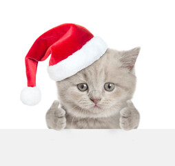 Aufkleber - Funny tiny kitten wearing red santa hat looking above blank white banner and showing thumbs up gesture. isolated on white background