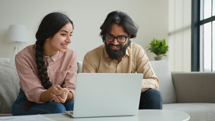 Wall Mural - Smiling Arabian Indian business couple muslim man woman talk online video call webcam laptop conference distant meeting at home office multiracial guy girl laughing friendly virtual chat in quarantine