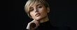 © Viacheslav - Thoughtful young woman with short blonde hair, wearing a black turtleneck, touching her chin in a contemplative pose against a dark backdrop. Concept of reflection and