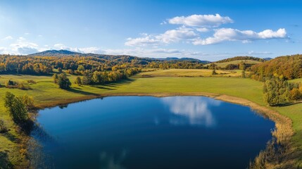 Canvas Print - Aerial view of serene rural marshland in autumn showcasing vibrant grasslands and a tranquil lake under a clear blue sky