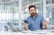 © Liubomir - Upset and disappointed man with phone in hands. Office worker at workplace looking anxiously at camera, working with laptop inside office at workplace.