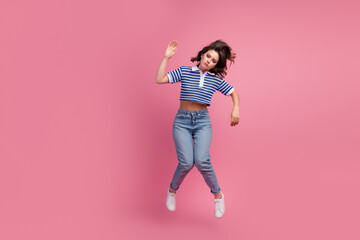 Wall Mural - Young woman in striped top and jeans jumping with energy against a vibrant pink background, showing dynamic movement