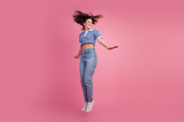 Young woman jumping with joy against a vibrant pink background, showcasing a playful mood and stylish attire