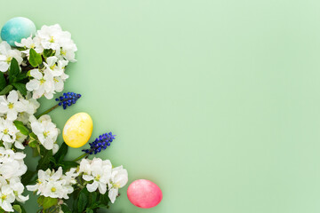 Spring Easter background, multi-colored Easter eggs and blooming apple tree branches and mint leaves and Muscari flowers on a green background, copy space