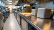 © pisan thailand - A modern commercial kitchen with stainless steel countertops, neatly stacked plates, and organized cooking equipment.