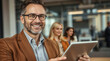 © PixelPulse AI - A smiling man holds a tablet in a photo likely for professional use. Two women are visible in the background, also with smiles