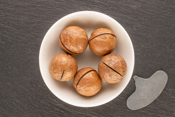 Wall Mural - Macadamia nuts in shell with ceramic saucer on slate stone, top view.