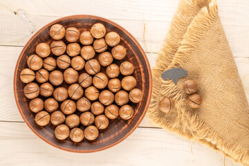 Wall Mural - Macadamia nuts in shell with clay plate and jute napkin on wooden table, top view.