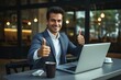 © nsit0108 - Happy businessman showing thumbs up gesture while working on laptop in a cafe