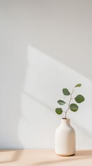 Fototapete - Sunlight streaming through window creates beautiful shadows on white wall behind eucalyptus leaves in simple white vase on wooden table, creating minimalist and modern kitchen decor