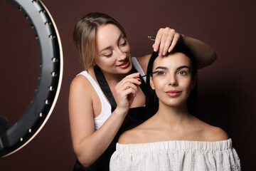 Wall Mural - Professional makeup artist working with beautiful young woman against brown background. Using ring lamp