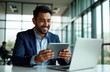 © Pete - Smiling Hispanic businessman uses tablet computer in modern office. He is working with laptop. Business suit. Happy man. Modern workplace. Tech and business environment. Confident pro.