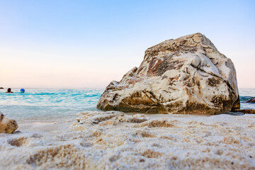 A large rock sits on a beach with a clear blue sky above