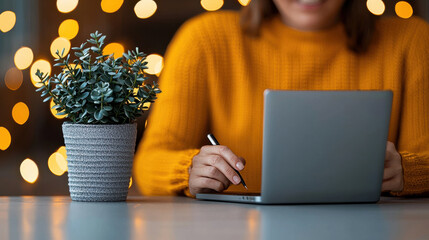 Fototapete - person in cozy sweater works on laptop, surrounded by warm bokeh lights and potted plant, creating productive and inviting atmosphere