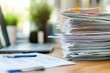 © SY - A large stack of papers sits on a desk near a laptop. Illustrates the concept of paperwork, deadlines, and office work.
