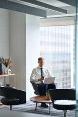 Wall Mural - Busy professional business man executive, young businessman manager wearing tie using smartphone and laptop technology working at office coworking lobby near big skyscraper window. Vertical photo.