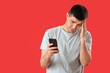 © Pixel-Shot - Sad young man with smartphone on red background