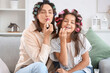 © Pixel-Shot - Little girl and her mother with hair curlers applying lipsticks at home