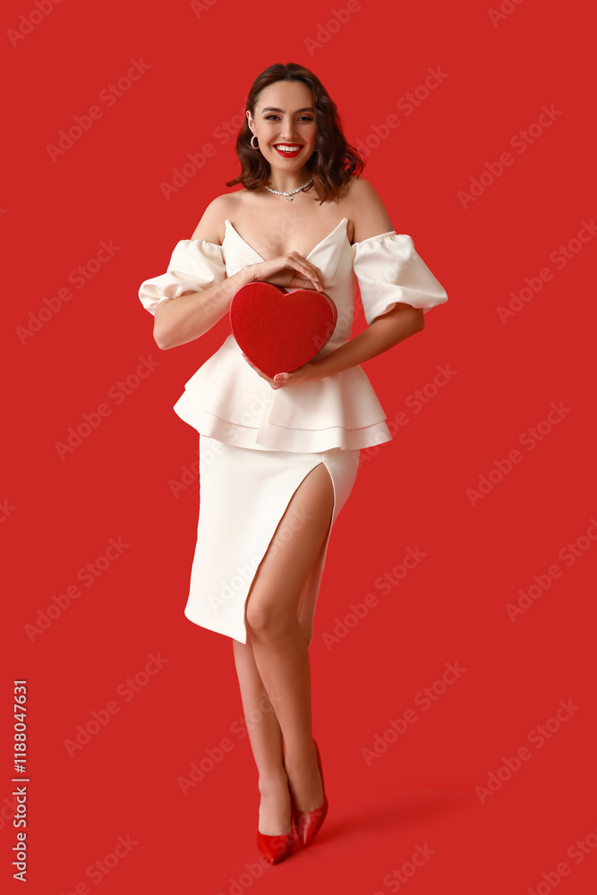 Happy young woman with heart shaped gift box on red background