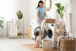 © Pixel-Shot - Young woman and her daughter pulling out clothes from washing machine at home