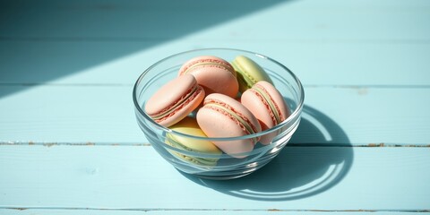 Wall Mural - A Glass Bowl Filled With Colorful Macarons Resting On A Light Blue Wooden Table With Sunlight Casting A Shadow