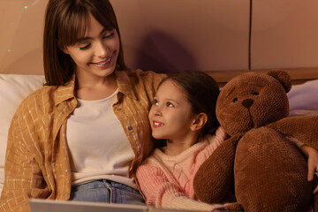 Canvas Print - Young mother reading story to her little daughter with toy bear in bedroom at night