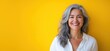 © Vergiliy - Smiling woman with gray hair against vibrant yellow background, showcasing confidence and beauty in aging, wearing white shirt, natural light, copy space for text