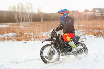 Riding a motorcycle in winter off-road. An enduro motorcyclist rides through a snowy field.