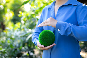 An image of lush green nature spreading across the scene, with vibrant trees and plants surrounding every corner. A person, either a man or a woman, stands at the center, holding an object in their ha