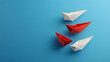 © mahamad - Group of white paper ships all moving in one direction, with one red paper ship going the opposite way, symbolizing innovative solutions
