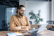 © Liubomir - A professional man sits at a desk in an office, intently working on his laptop. The workspace displays a calm and productive atmosphere, reflecting a professional and focused setting.