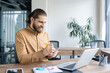 © Liubomir - Smiling businessman working at a desk, writing in a notebook with a laptop nearby. Ideal for concepts of productivity, business planning, and professional work environments.