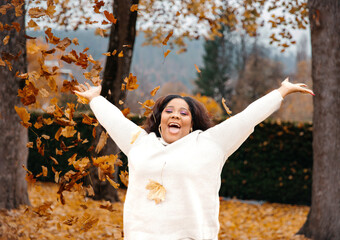 Wall Mural - Joyful african female enjoying autumn leaves in park