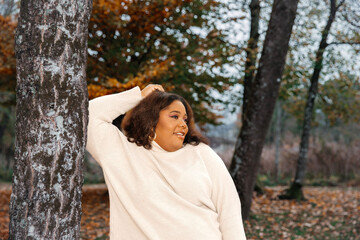 Wall Mural - Content hispanic young female in autumn forest wearing cream sweater