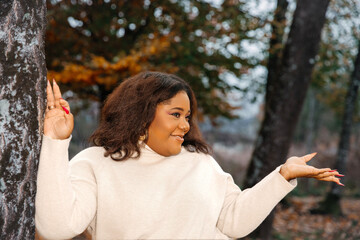 Wall Mural - Smiling african female in autumn forest, young woman in white sweater, enjoying nature