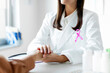 © Home-stock - Oncology and breast cancer concept. Woman doctor with pink awareness ribbon talking with female patient at hospital during visit, closeup