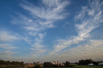 Breathtaking wispy clouds stretch across a vibrant sky near a serene countryside landscape