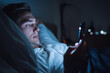 © ASSIASIA - A sleepless man is lying in bed and doom scrolling on cellphone during bedtime