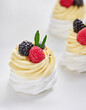© Food Images - Swirls of light meringue and rich cream form delicate peaks, elegantly adorned with vibrant blackberries and raspberries, creating an inviting dessert display