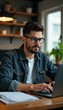 © SuriyaPhoto - A focused young man working on a laptop at a stylish desk with plants.
