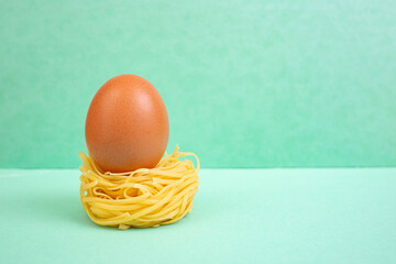 Raw whole egg on a rolled pasta nest on bright green background