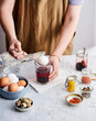 © Food Images - A person is using a spoon to dip an egg into a jar of beet dye, surrounded by various jars of spices and other ingredients on a countertop. The setting is bright and inviting