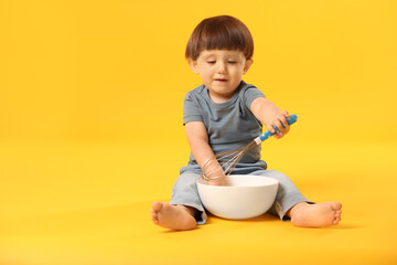 Wall Mural - Cute little boy with bowl and whisk on yellow background. Space for text