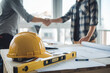 © FATNA - yellow safety helmet on workplace desk with construction worker team hands shaking greeting start up plan new project contract in office center at construction site, partnership and contractor concept