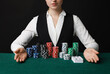 © New Africa - Professional croupier with casino chips and playing cards at gambling table on black background, closeup