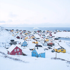 Picturesque small town surrounded by snow-covered mountains and pristine icy landscapes, vibrant houses contrasting with serene white snow under a clear Arctic sky