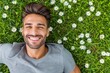 © kornc - A man is smiling and laying on the grass next to a field of daisies