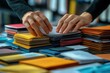 © Vadym - Close-up view of hands arranging colorful marketing materials on desk. Business adviser reviewing, refining client marketing collateral. Focus on meticulous organization, selection of various print